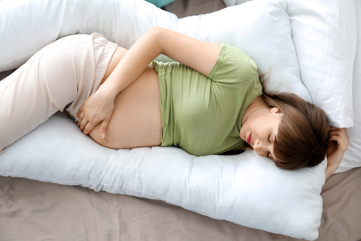 Young pregnant woman sleeping on maternity pillow at home