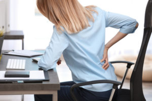 Young woman suffering from back pain in office